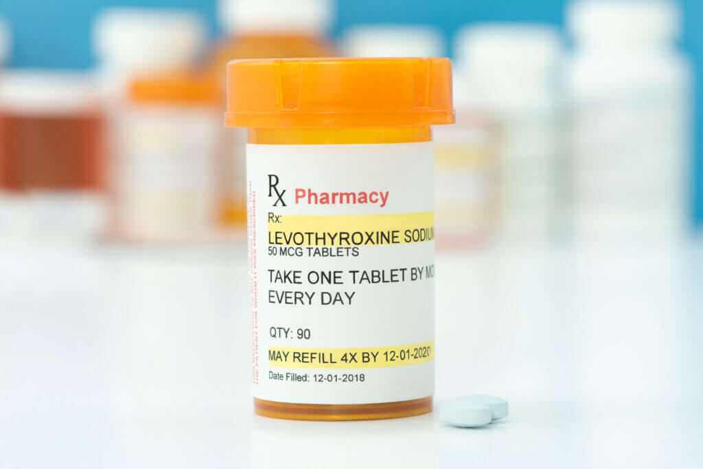 Prescription bottle of levothyroxine sitting on a countertop with two pills sitting to the right of the bottle.